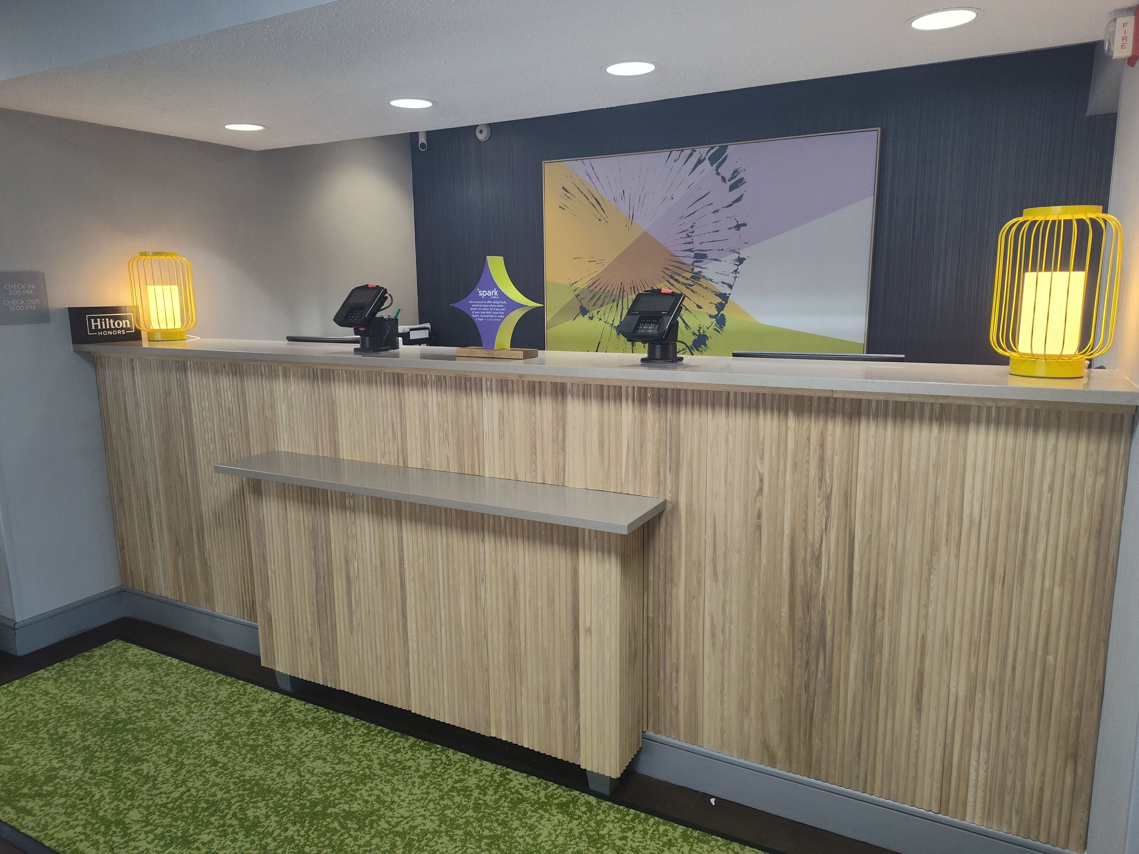 A hotel reception desk with a wooden finish, a green carpet, and two illuminated wall sconces.