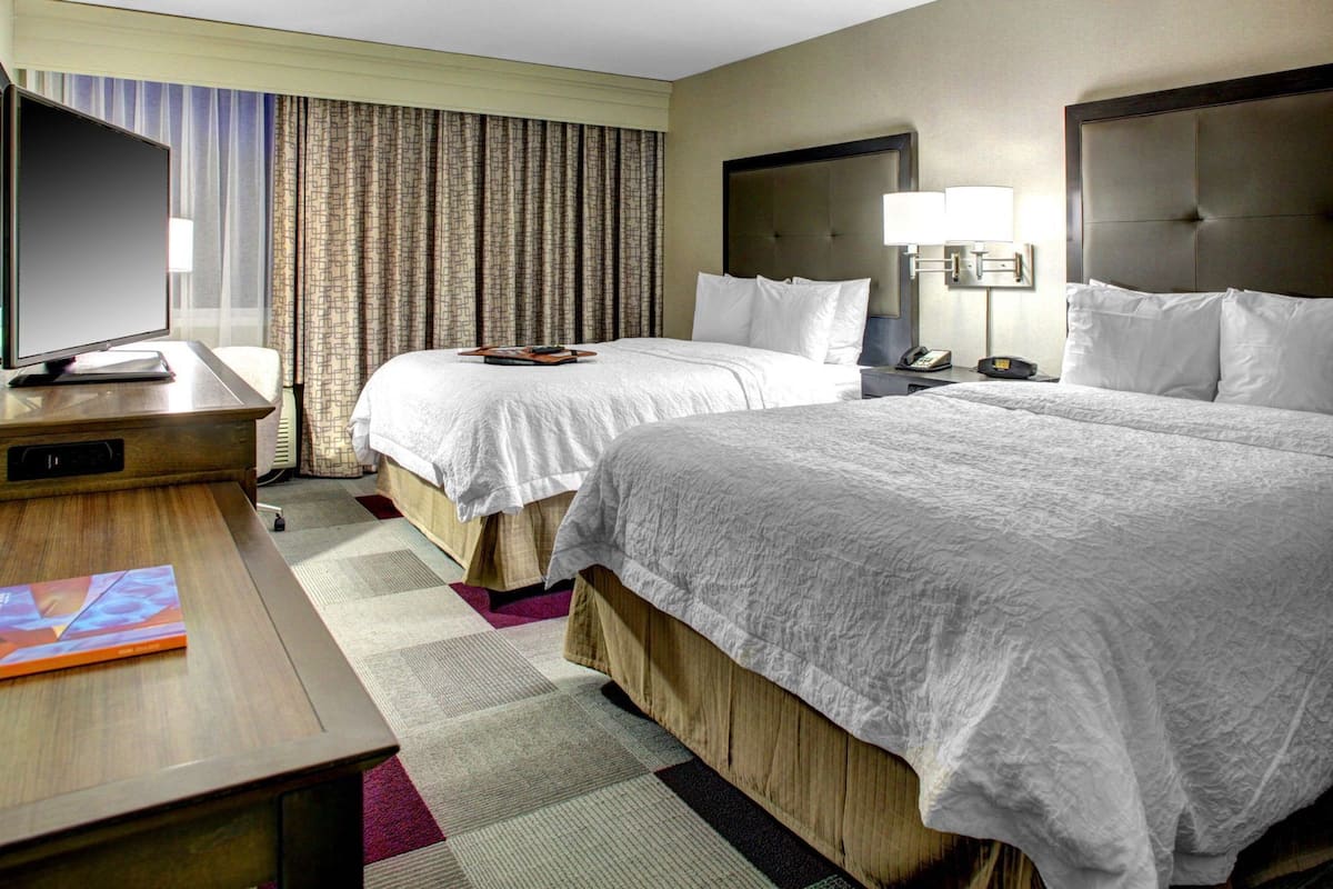 A hotel room with two beds, a desk with a TV, a lamp, and a patterned rug.