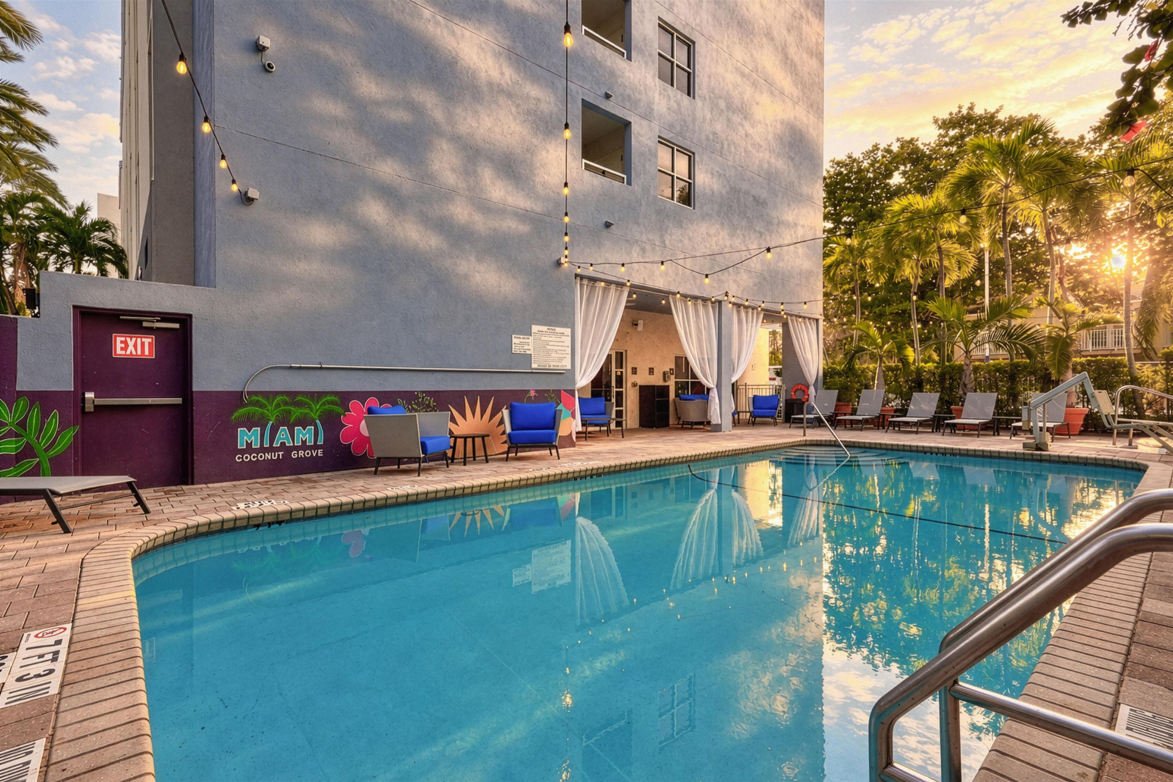 A swimming pool with a view of a building with a sign reading 'Coconut Grove' and a door marked 'EXIT'.