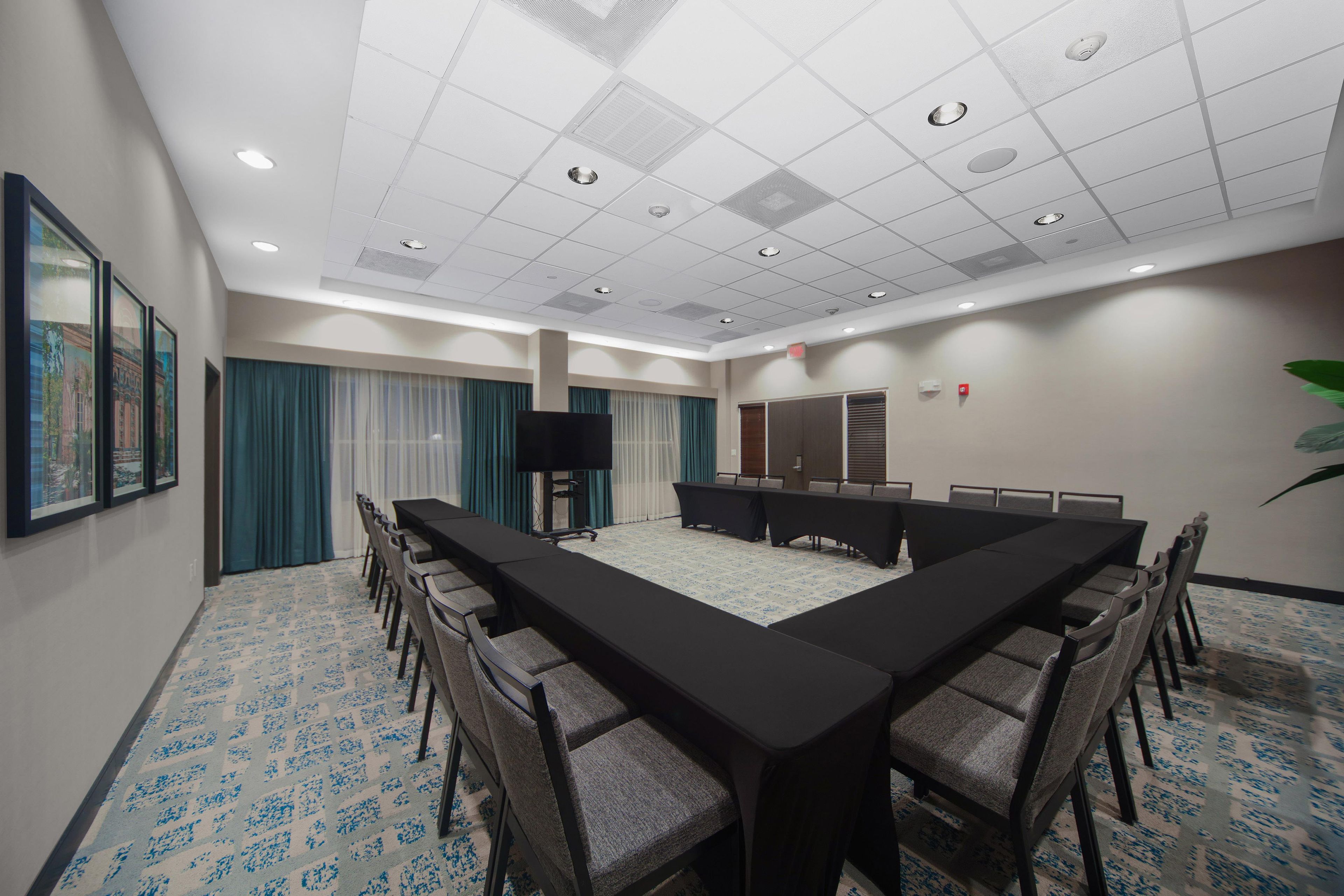 A conference room with a long table, chairs, a flat-screen TV, and a patterned carpet.