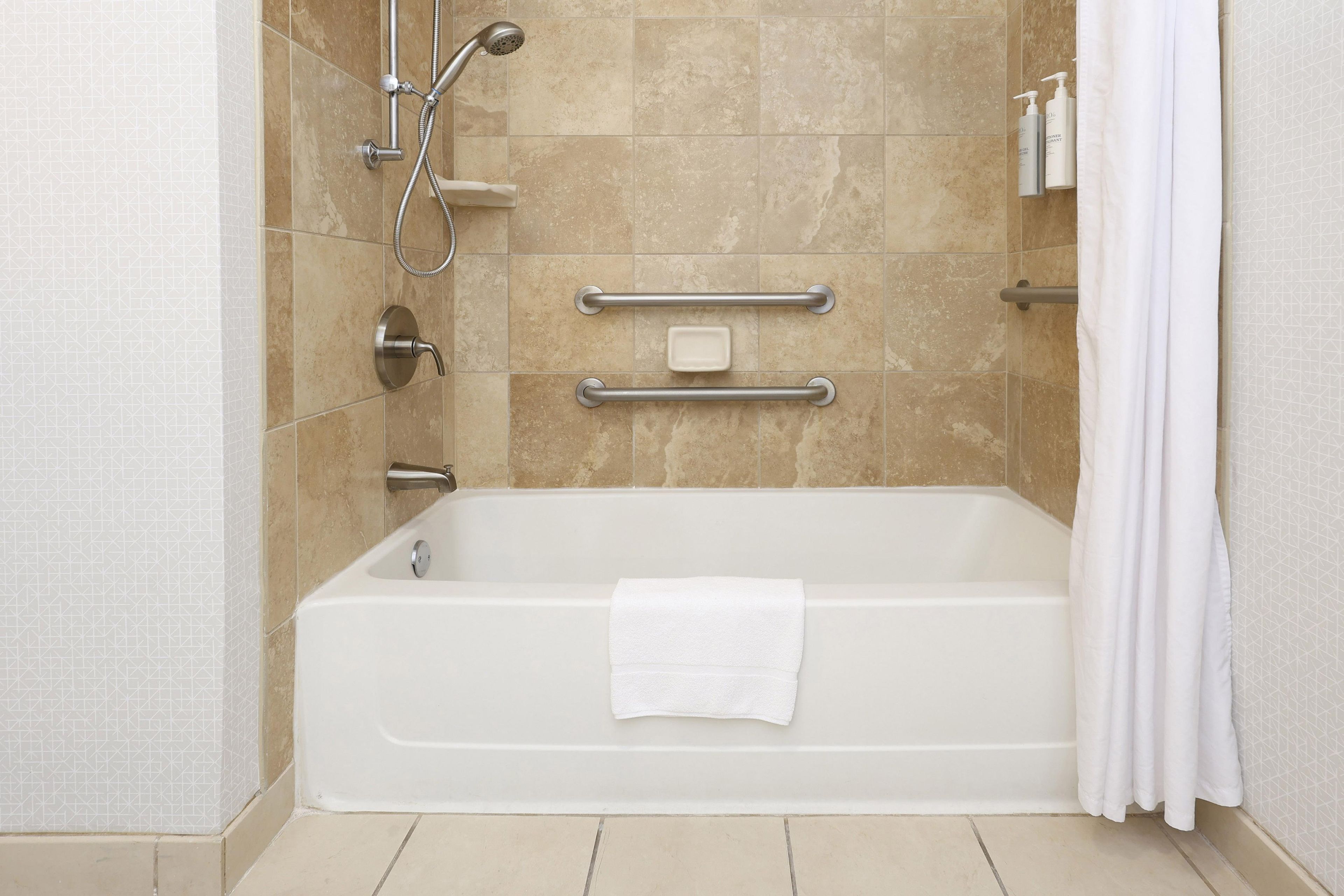 A modern bathroom with a bathtub, grab bars, a handheld showerhead, and a towel.