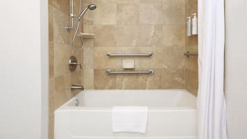 A modern bathroom with a bathtub, grab bars, a handheld showerhead, and a towel.