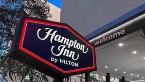 Señal de Hampton Inn by Hilton con vista clara de la entrada del edificio y un letrero de 'Bienvenido' encima.