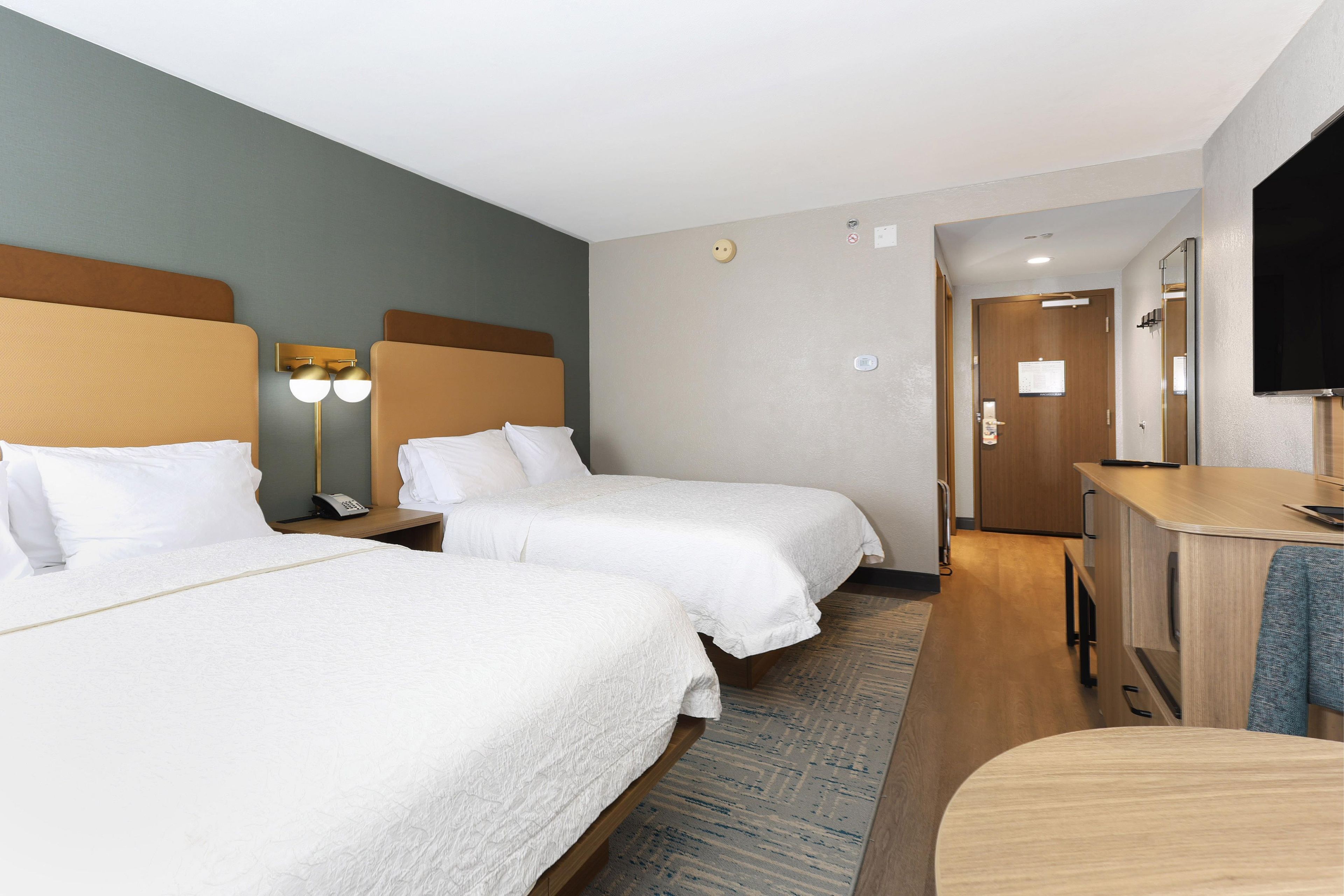 A hotel room with two beds, a desk, a mirror, and a door leading to a bathroom.