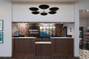 Un comptoir d’accueil orné d’une enseigne « Bienvenue à Hampton », d’un lustre moderne et d’une fresque représentant un paysage urbain.