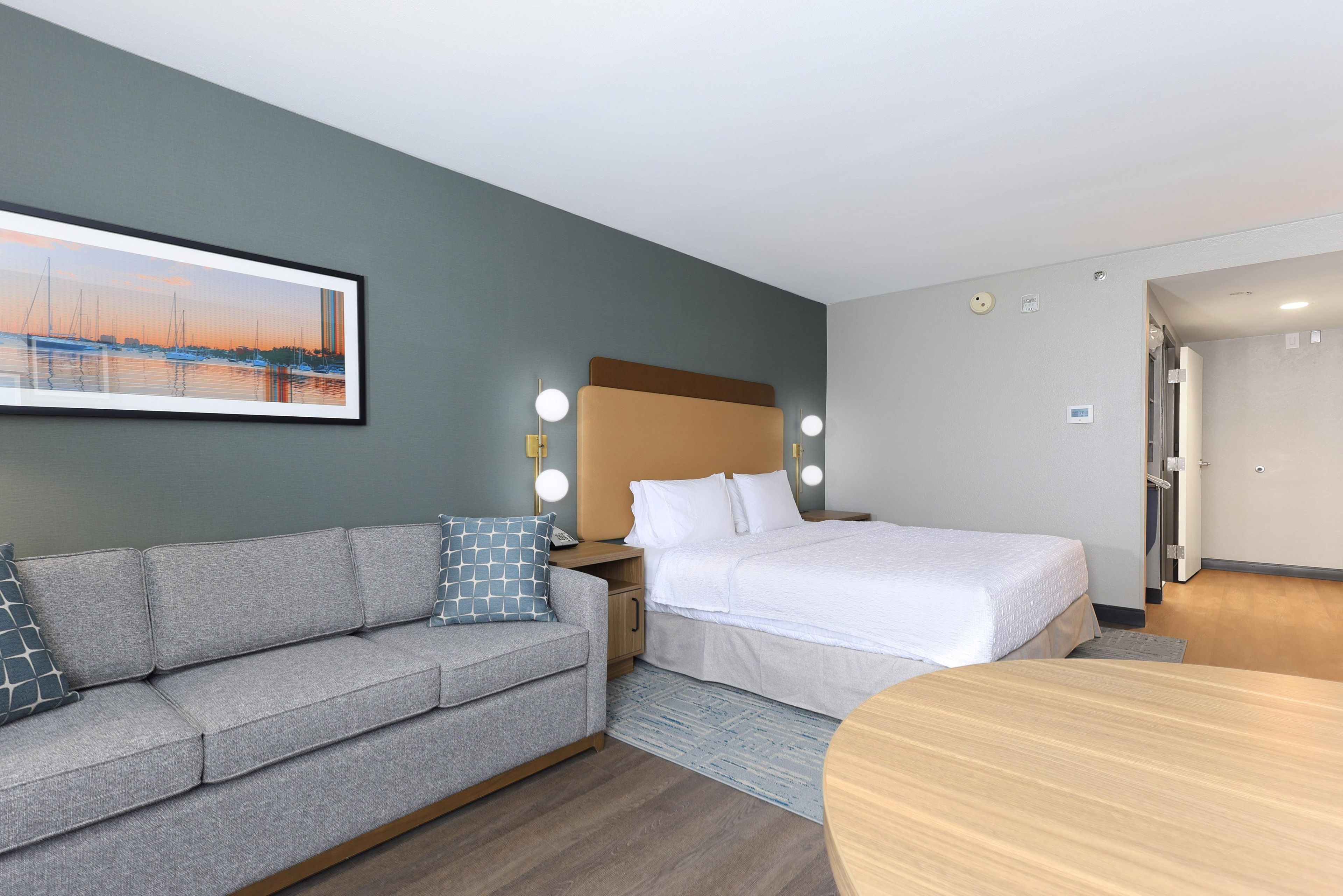 A hotel room with a bed, a sofa, a table, and a painting on the wall.