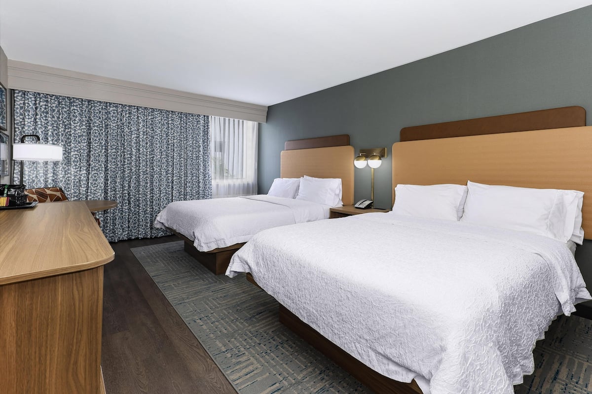 A hotel room with two beds, a desk, a lamp, and a nightstand.