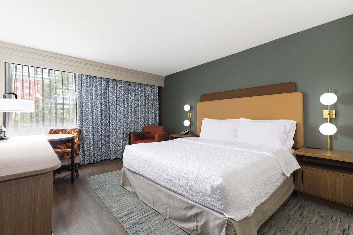 A hotel room with a bed, desk, chair, and a view of the outdoors.