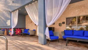 Un espacio al aire libre con sofás y sillones azules, cortinas blancas y luces colgantes.