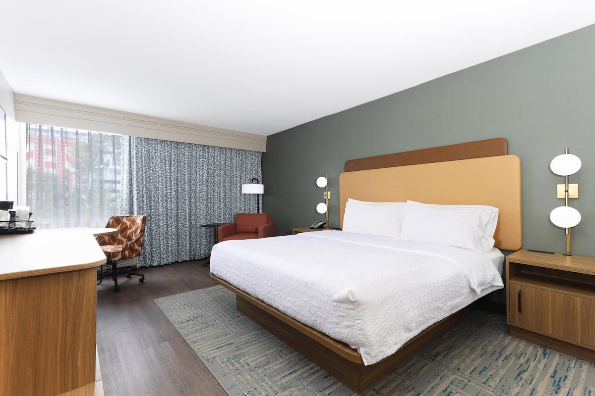 A hotel room with a large bed, a desk, a chair, and a nightstand with lamps.