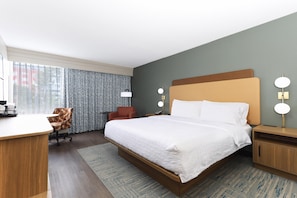 Una habitación de hotel con cama, escritorio, silla y mesita de noche con lámpara.