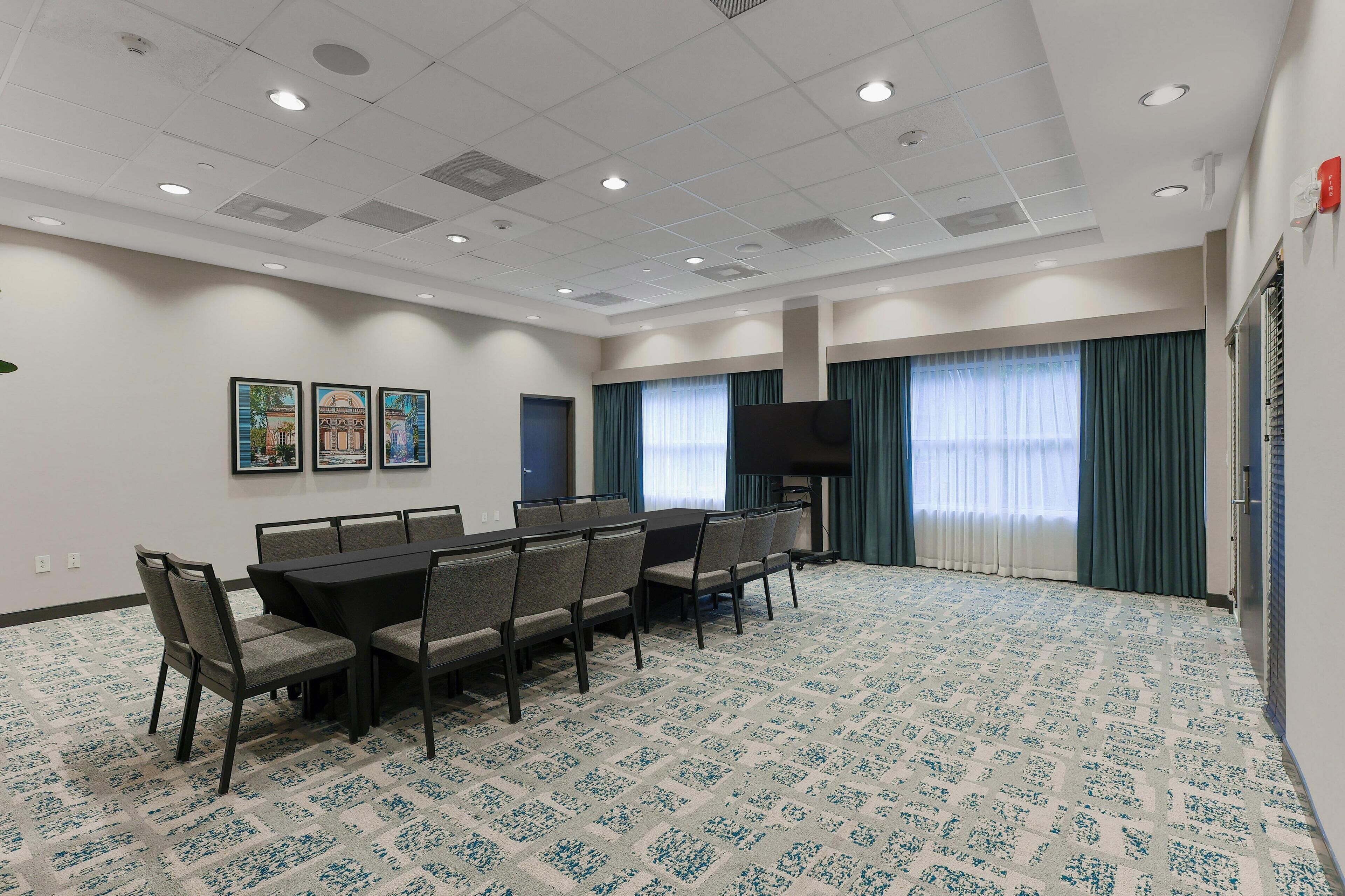 A conference room with a rectangular table, six chairs, a flat-screen TV, and a patterned carpet.