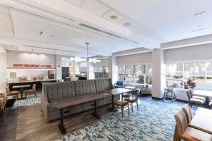 A modern restaurant with a central seating area, a bar, and large windows.