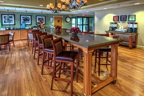 A spacious bar area with wooden chairs and a central island, equipped with coffee machines and a clock on the wall. - Hampton Inn by Hilton Charlotte/Matthews (Matthews)