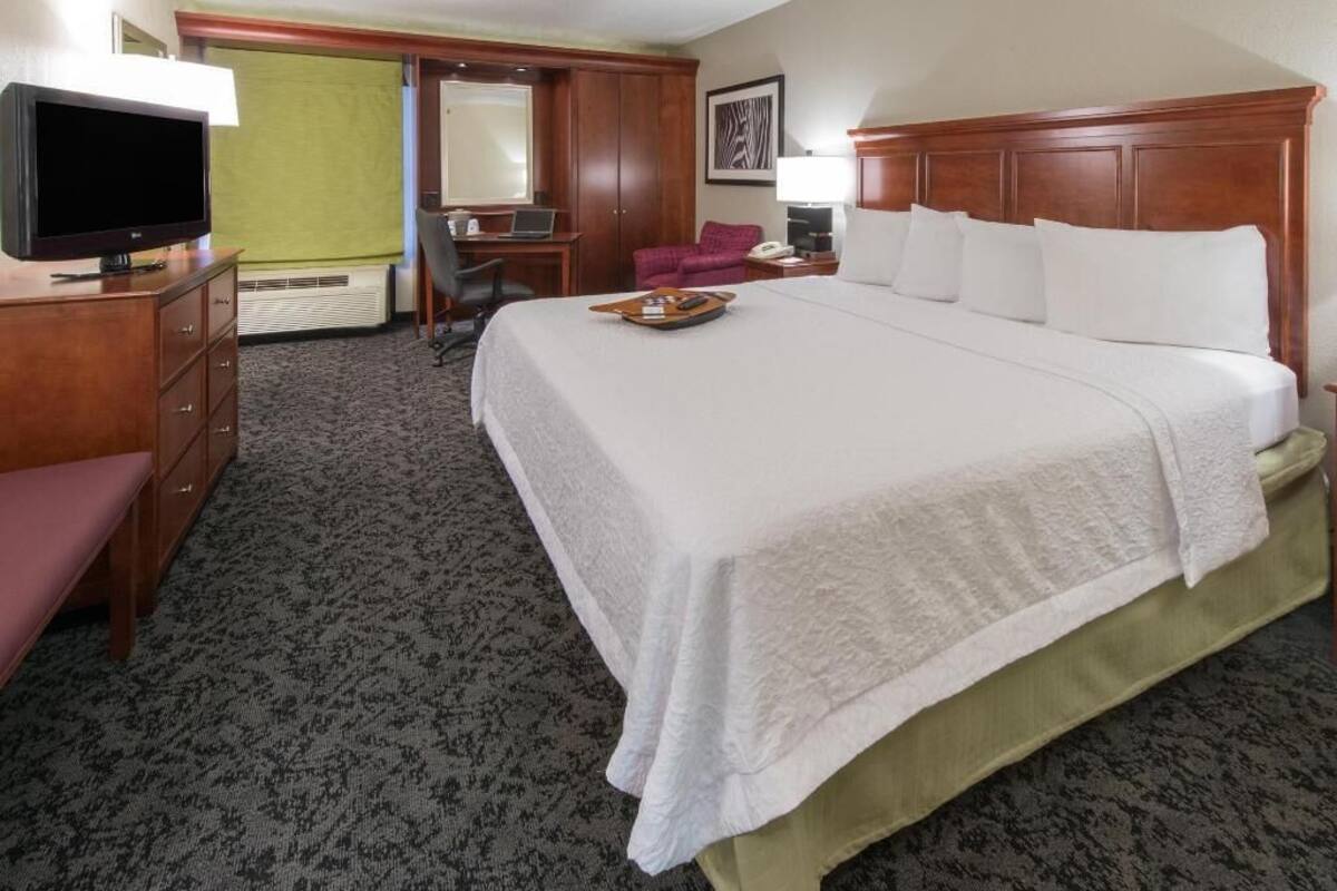 A hotel room with a large bed, a television, a desk with a chair, and a mirror.