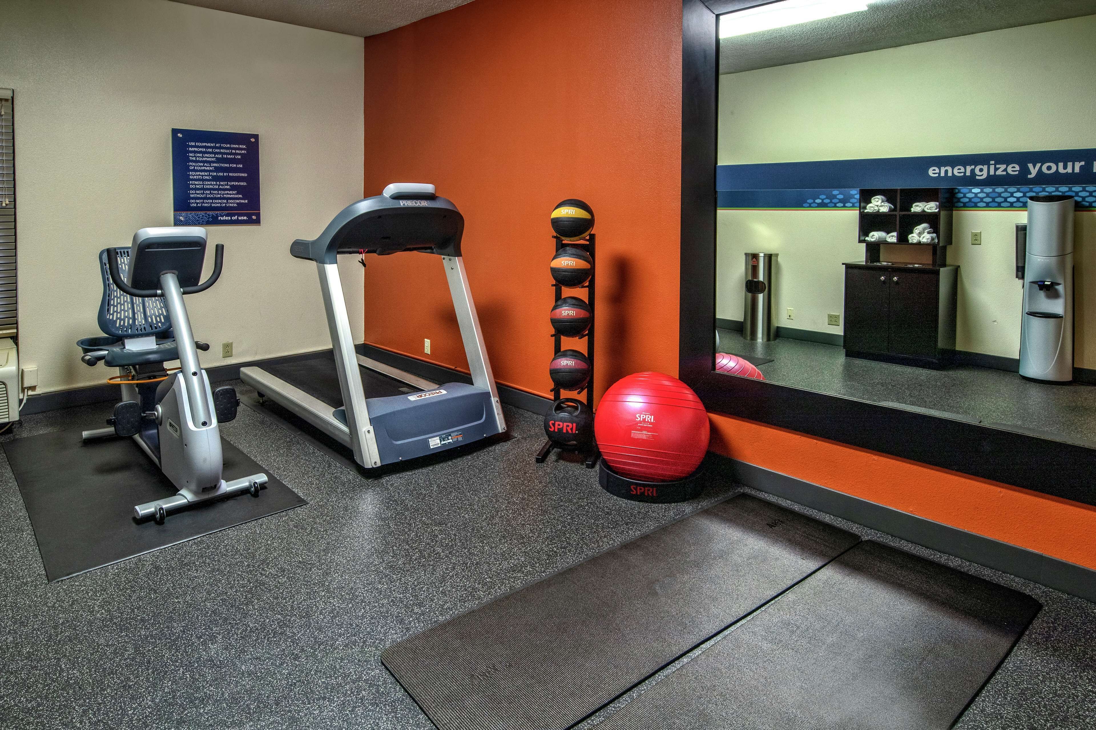 Un gimnasio con cinta de correr, elíptica y un soporte de pared para balones medicinales.
