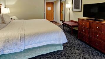 A hotel room with a large bed, a wooden dresser, a television, and a mirror.