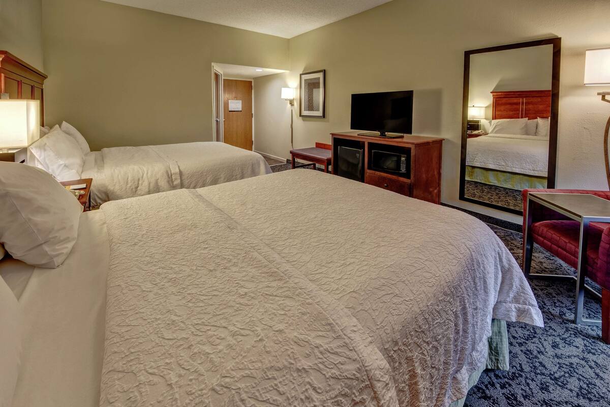 A hotel room with two beds, a television, a desk, and a mirror.