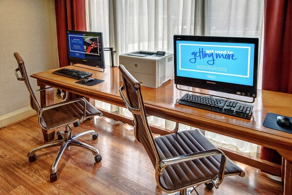 A hotel conference room with a wooden desk, two office chairs, a desktop computer, a laptop, and a printer. - Hampton Inn by Hilton Charlotte/Matthews (Matthews)