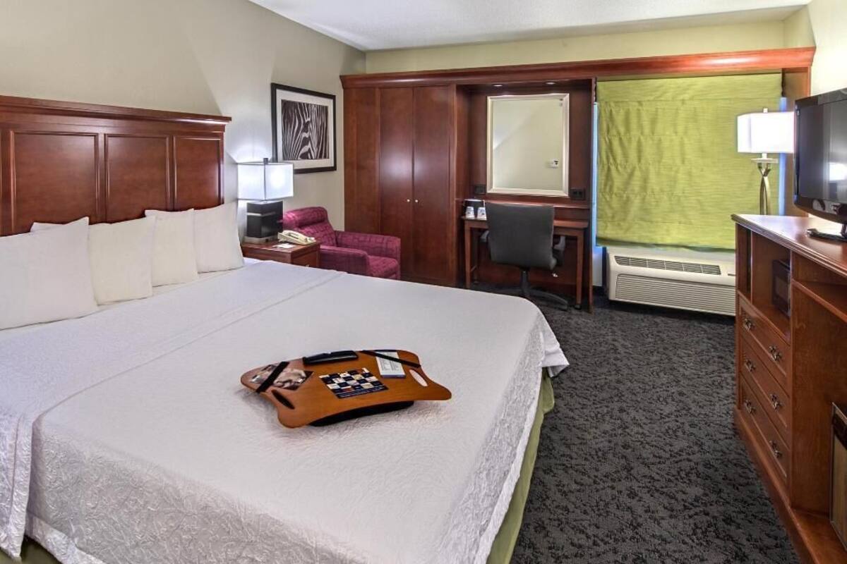A hotel room with a large bed, a desk, a chair, a television, and a dresser.