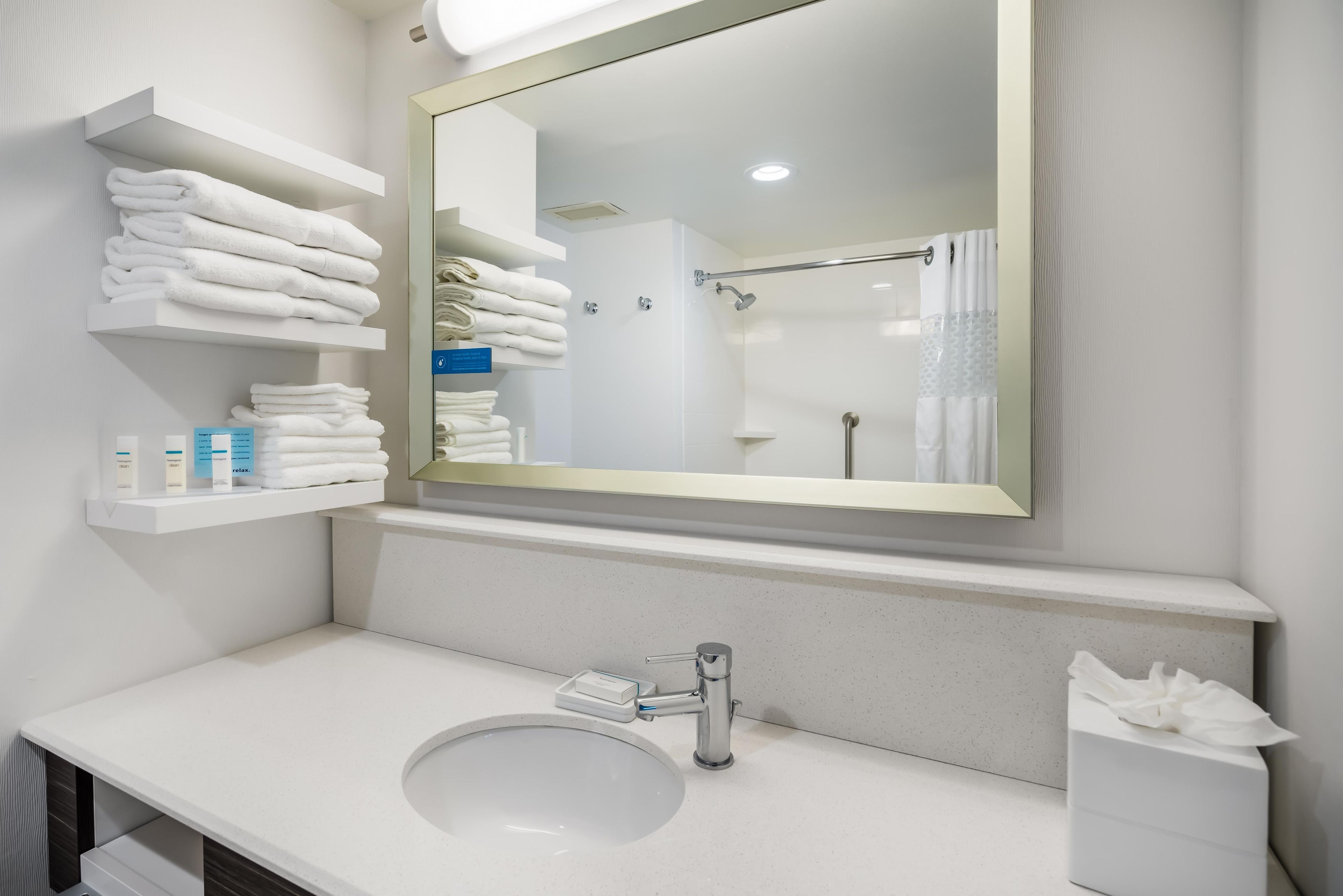 A modern bathroom with a white sink, a large mirror, and shelves with neatly folded towels.
