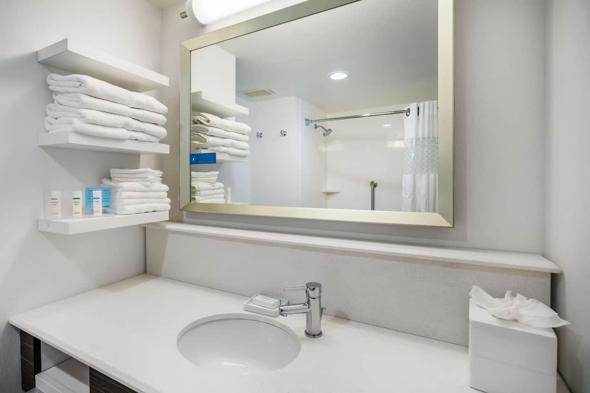 A modern bathroom with a large mirror, white sink, and towel storage.