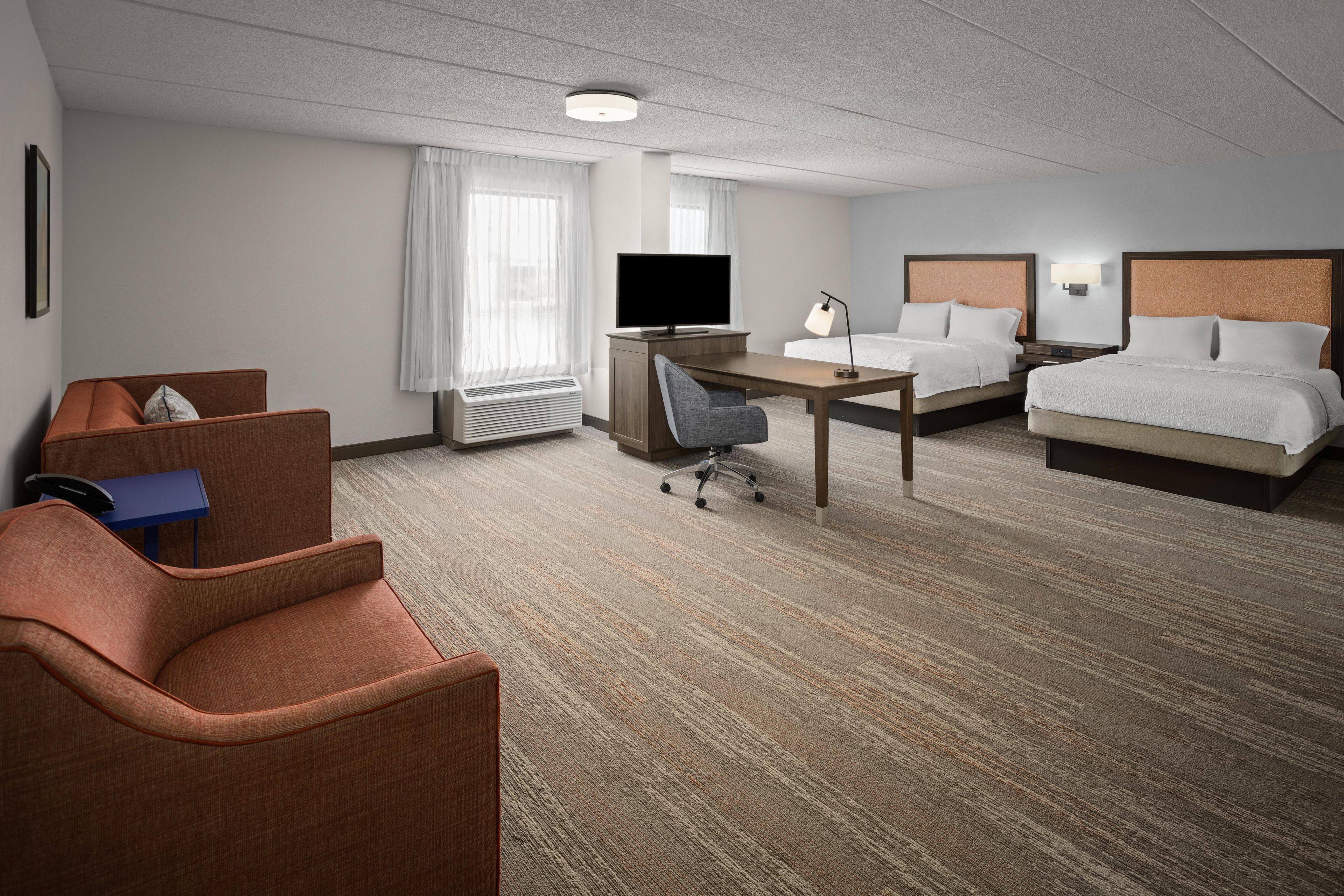 Habitación de hotel con cama, escritorio, silla, televisión y ventana con cortinas.