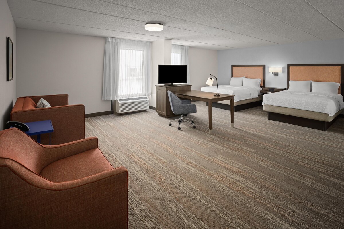 Een hotelkamer met een bed, een bureau, een stoel, een televisie en een raam met gordijnen.