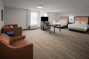 Habitación de hotel con cama, escritorio, silla, televisión y ventana con cortinas.