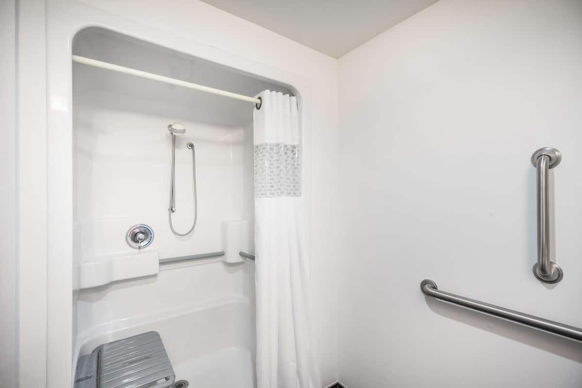 A bathroom with a shower, grab bars, and a towel rack.