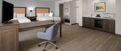 Habitación de hotel con cama, escritorio, silla, televisión y baño con ducha e inodoro.