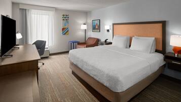 A hotel room with a large bed, a desk, a chair, a TV, and a window with curtains.