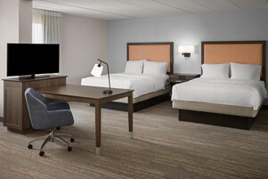 A hotel room with a desk, two beds, a TV, and a chair.
