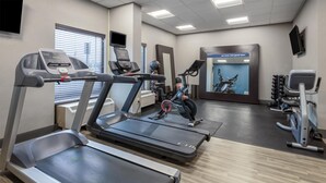 Ein Fitnessraum mit Laufbändern, Fahrrädern und einer Spiegelwand.