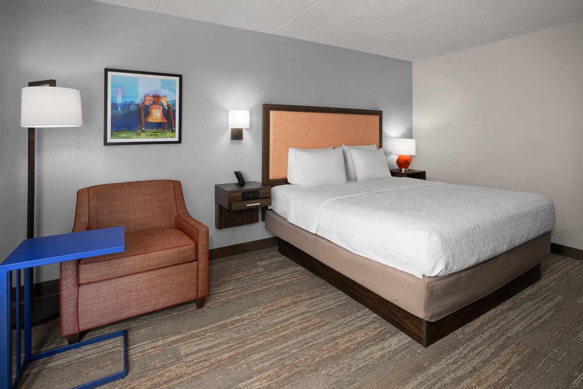Een hotelkamer met een bed, een stoel, een bureau en een nachtkastje met een lamp.