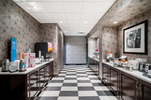 A hotel kitchen with checkered flooring, patterned wallpaper, and various kitchen appliances and supplies. - Hampton Inn Dover (Dover)