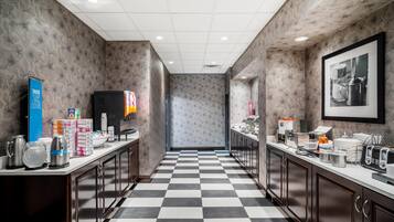 A hotel kitchen with checkered flooring, stainless steel appliances, and a framed photograph on the wall.