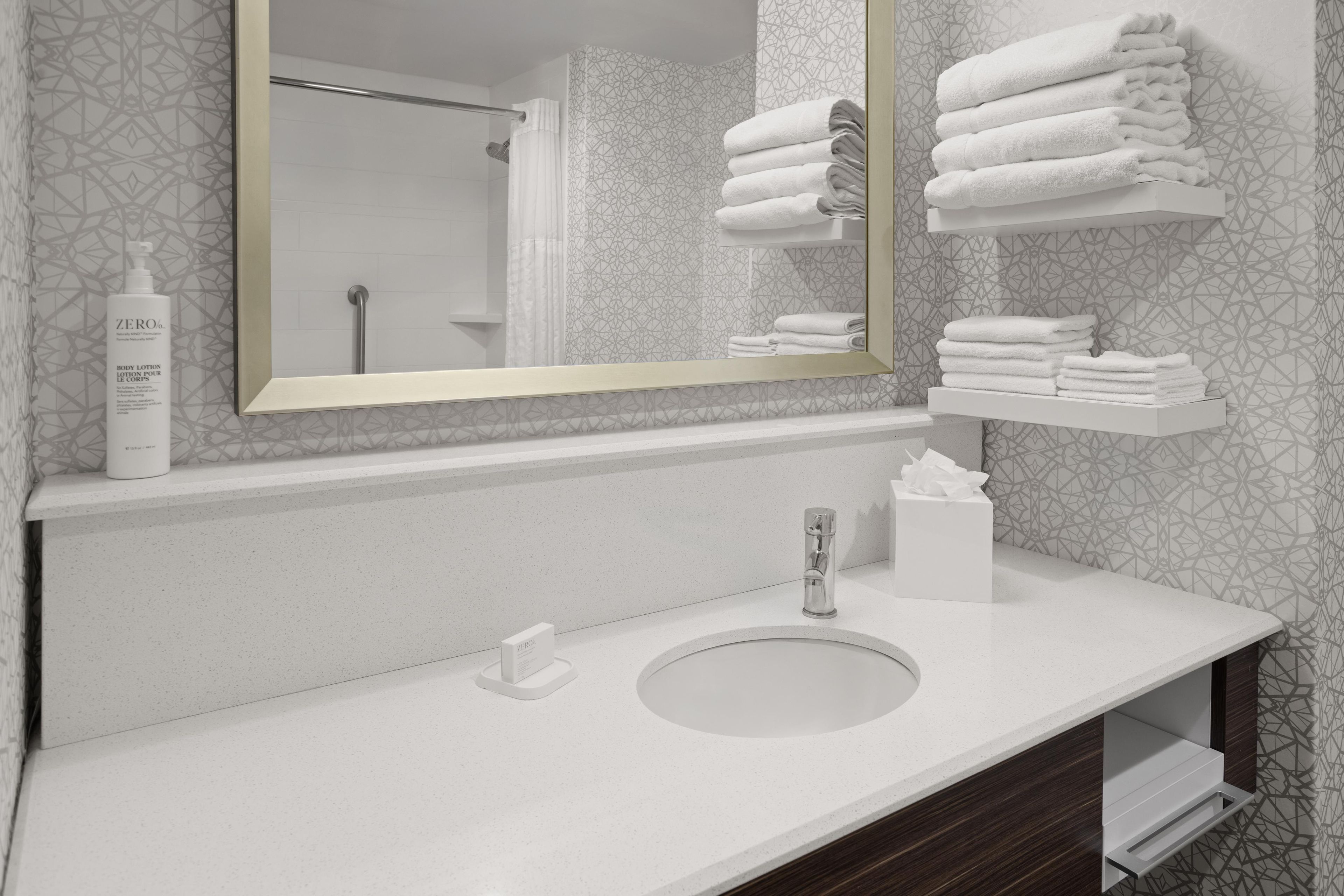 A bathroom with a large mirror, a sink, a towel rack, and a bottle of body lotion.