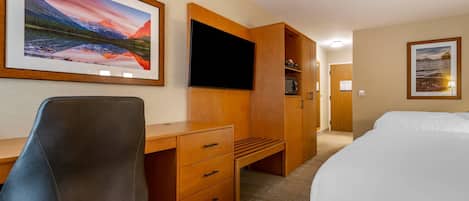 A hotel room with a bed, a desk with a chair, a television, and artwork on the walls.