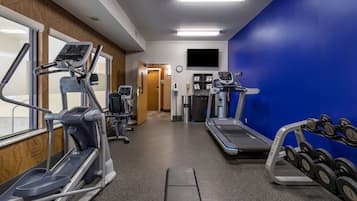 A gym with treadmills, elliptical machines, and a weight bench with dumbbells.
