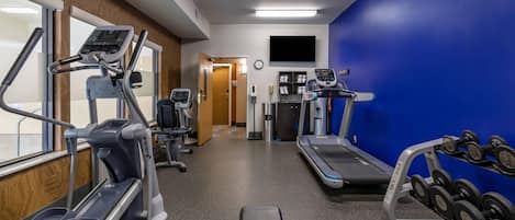 Un gimnasio con cintas de correr, elípticas y una banca de pesas con mancuernas.
