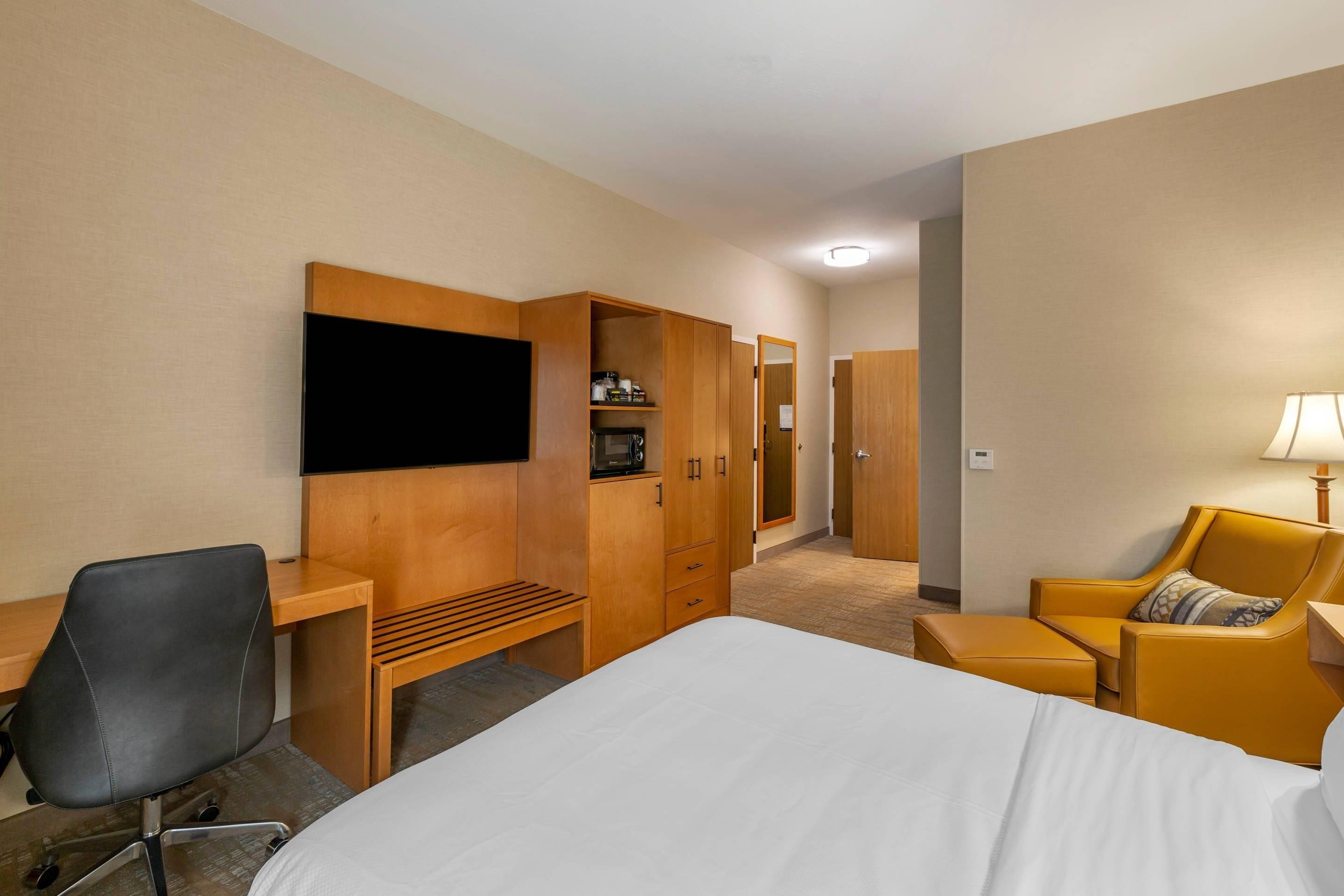 Ein Hotelzimmer mit Bett, Schreibtisch, Stuhl, Kleiderschrank und Fernseher.