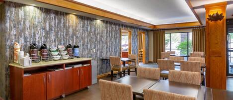 A hotel dining area with a buffet, seating arrangements, and a view through the windows.