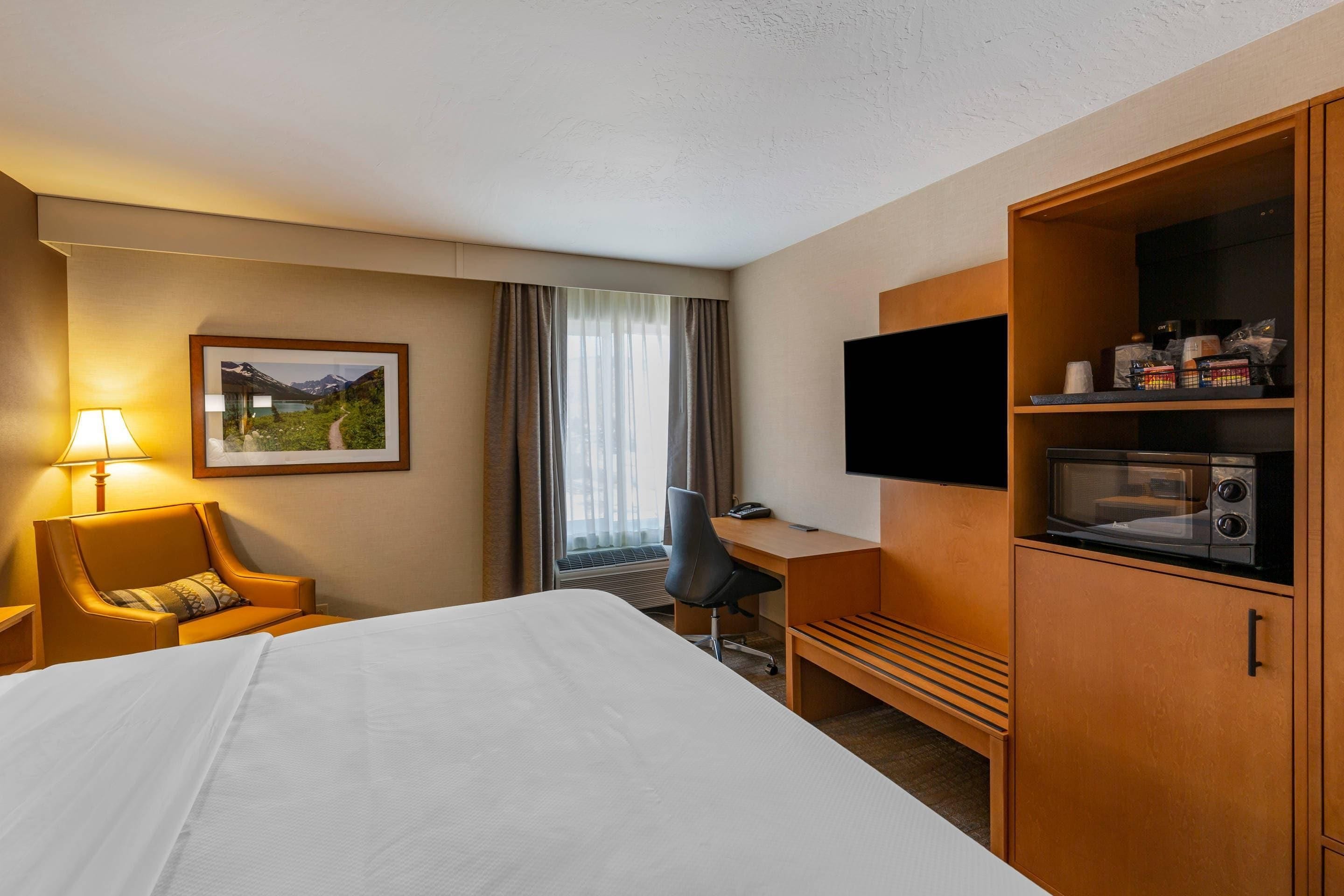 A hotel room with a bed, a desk, a chair, a television, and a microwave.