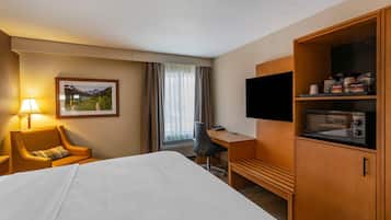 A hotel room with a bed, a desk, a chair, a television, and a microwave.