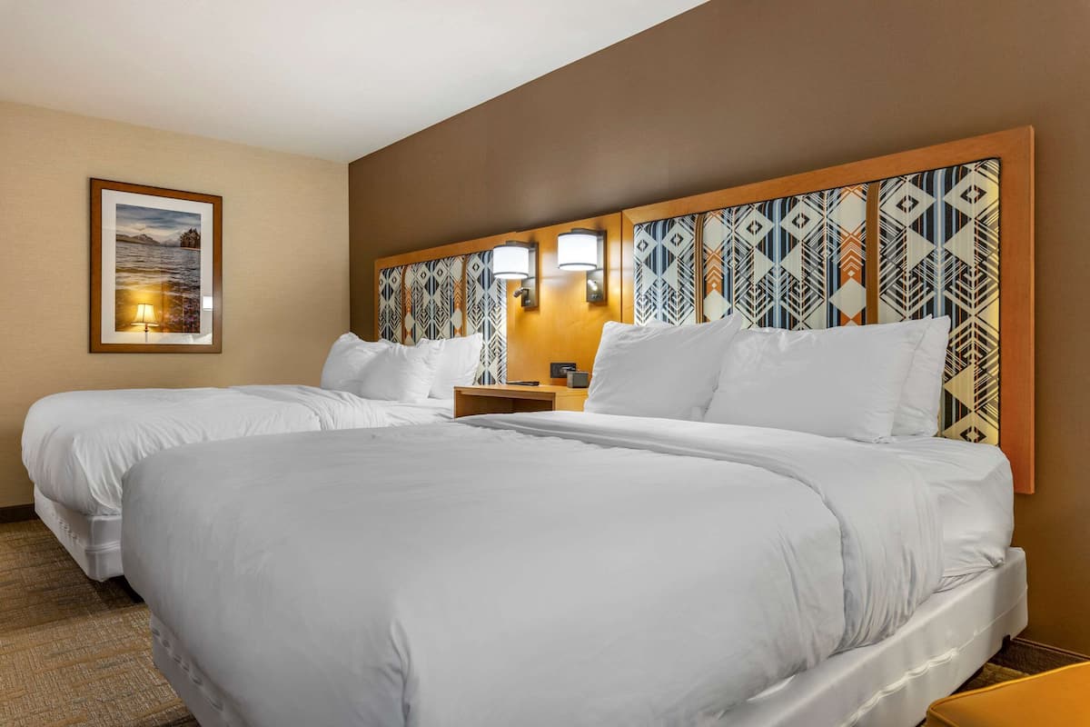 A hotel room with two beds, a headboard with a geometric pattern, a nightstand, and a framed picture on the wall.