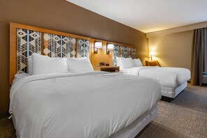 A hotel room with two beds, a headboard with a geometric pattern, bedside lamps, and a carpeted floor.