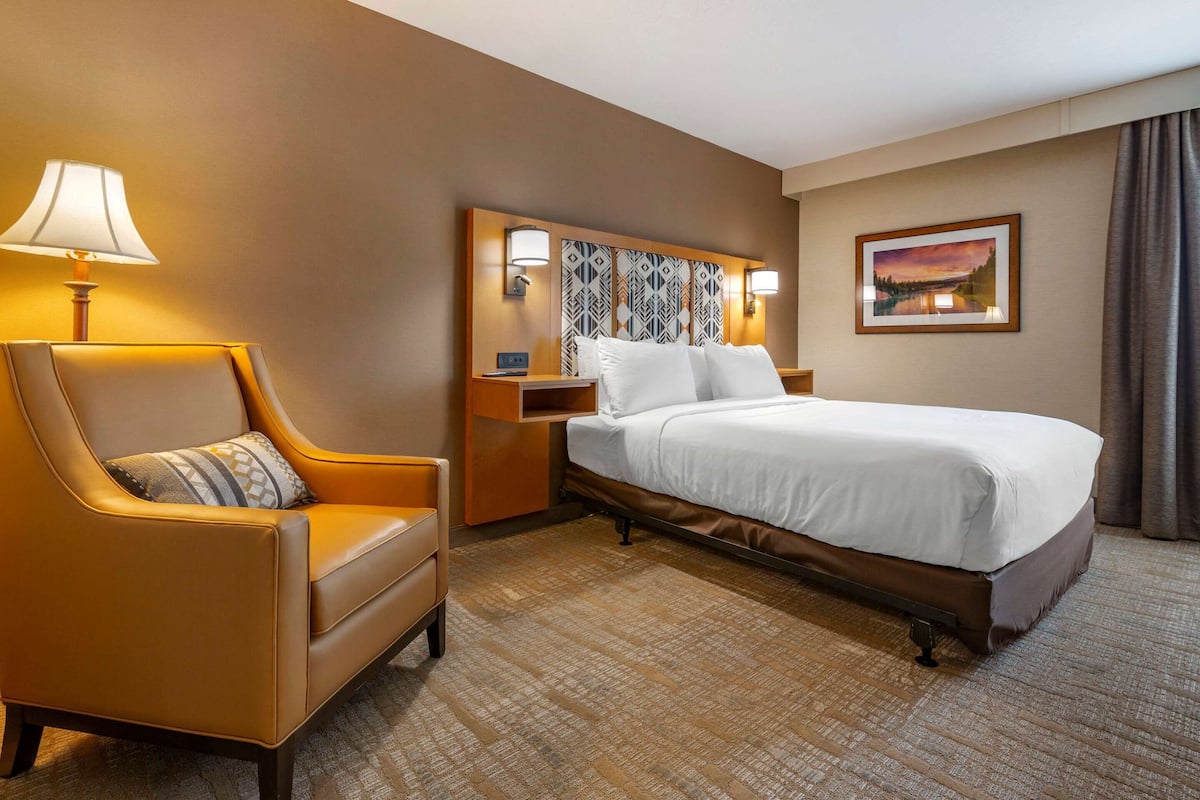 A hotel room with a bed, a chair, a nightstand, a lamp, and a painting on the wall.