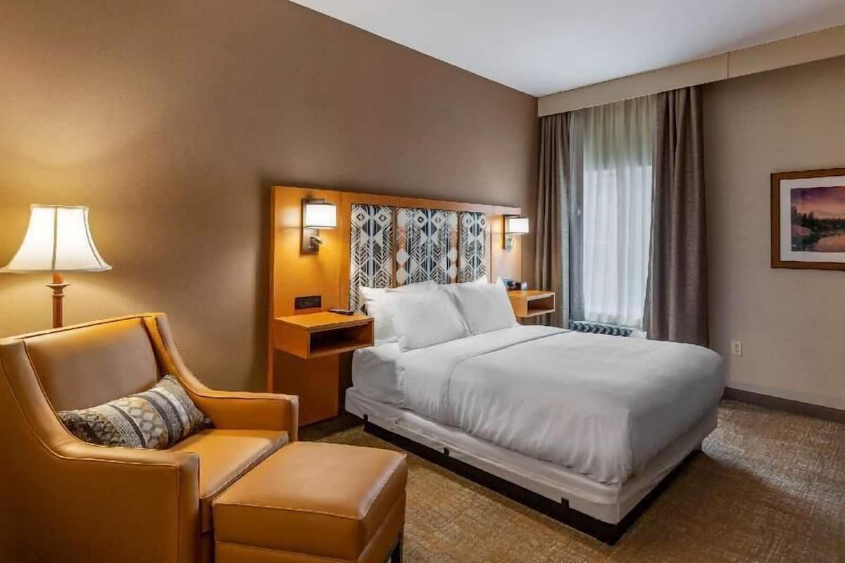 A hotel room with a large bed, a chair, a nightstand, and a lamp.