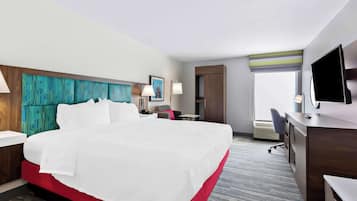 A hotel room with a large bed, a desk, a chair, a TV, and a window.